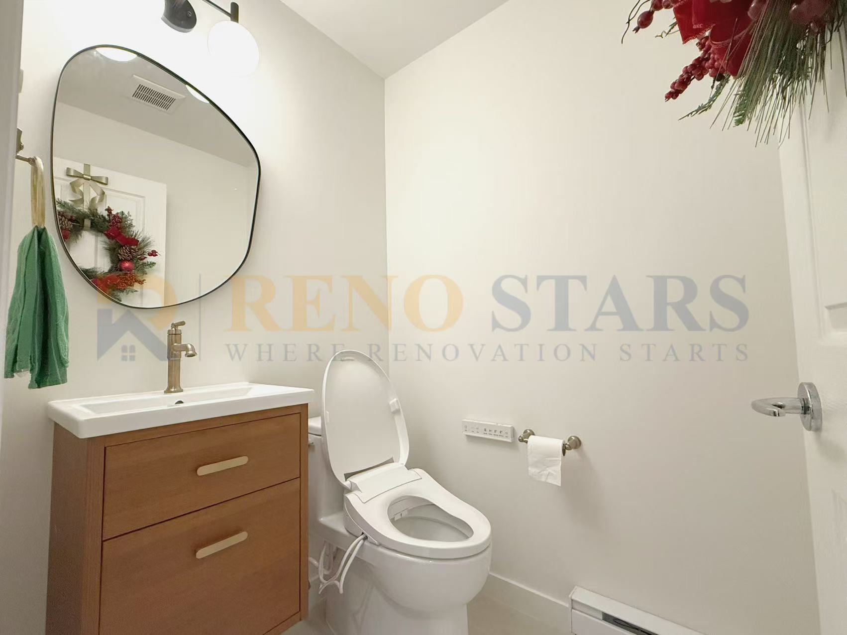 Modern bathroom featuring a wooden vanity, round mirror, and festive wreath decoration.