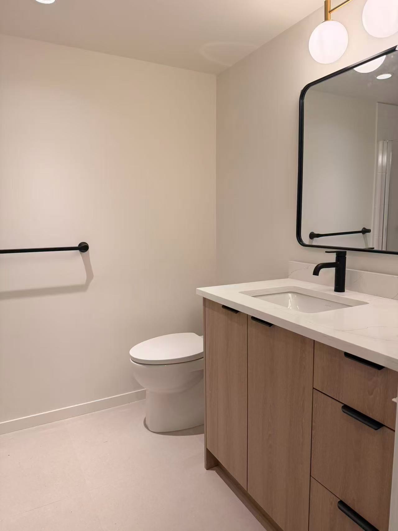 Modern bathroom featuring a wooden vanity, white toilet, and stylish mirror with lighting.