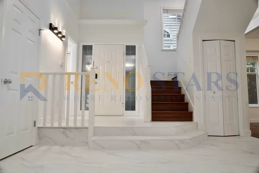Bright entryway featuring marble flooring, white walls, and wooden stairs leading to the upper level.