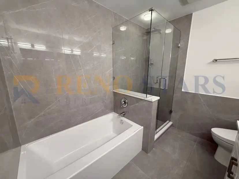 Modern bathroom featuring a glass shower, bathtub, and sleek gray tiles.